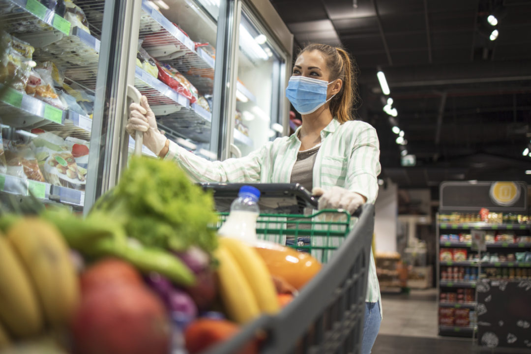 Woman grocery shopping while wearing face mask and gloves