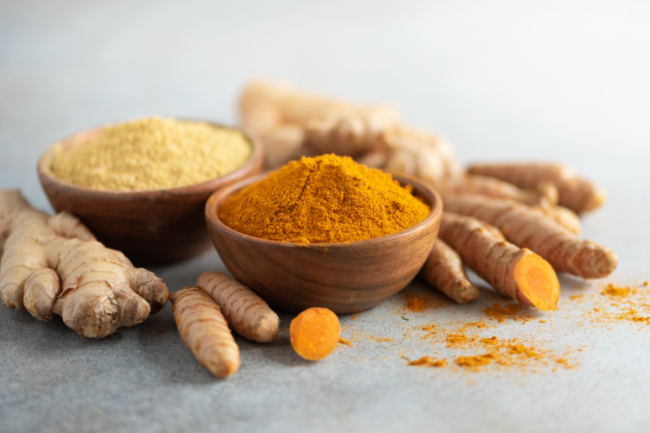 Turmeric and giger powder in wooden bowl and fresh turmeric root on grey concrete background.