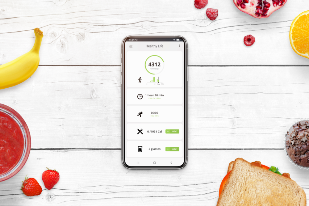 Phone on desk surrounded with food. Healthy life app concept with daily number of steps, number of calories burned, number of calories consumed