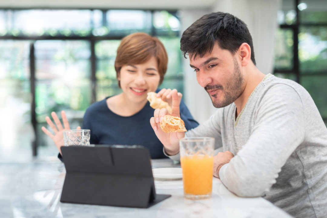 Couple eating at home while video calling friends