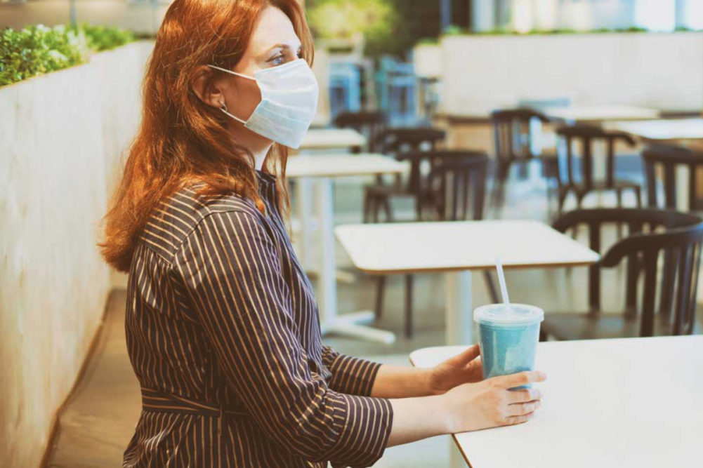 Woman wearing mask sitting inside restaurant with a drink