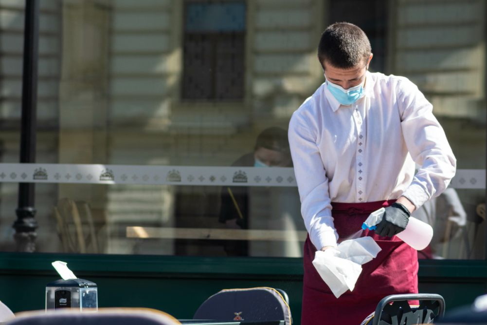 waiter wearing a face mask disinfecting tables