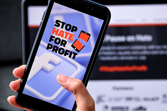 Stop Hate For Profit Logo on a cell phone screen in front of a computer