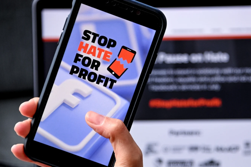 Stop Hate For Profit Logo on a cell phone screen in front of a computer
