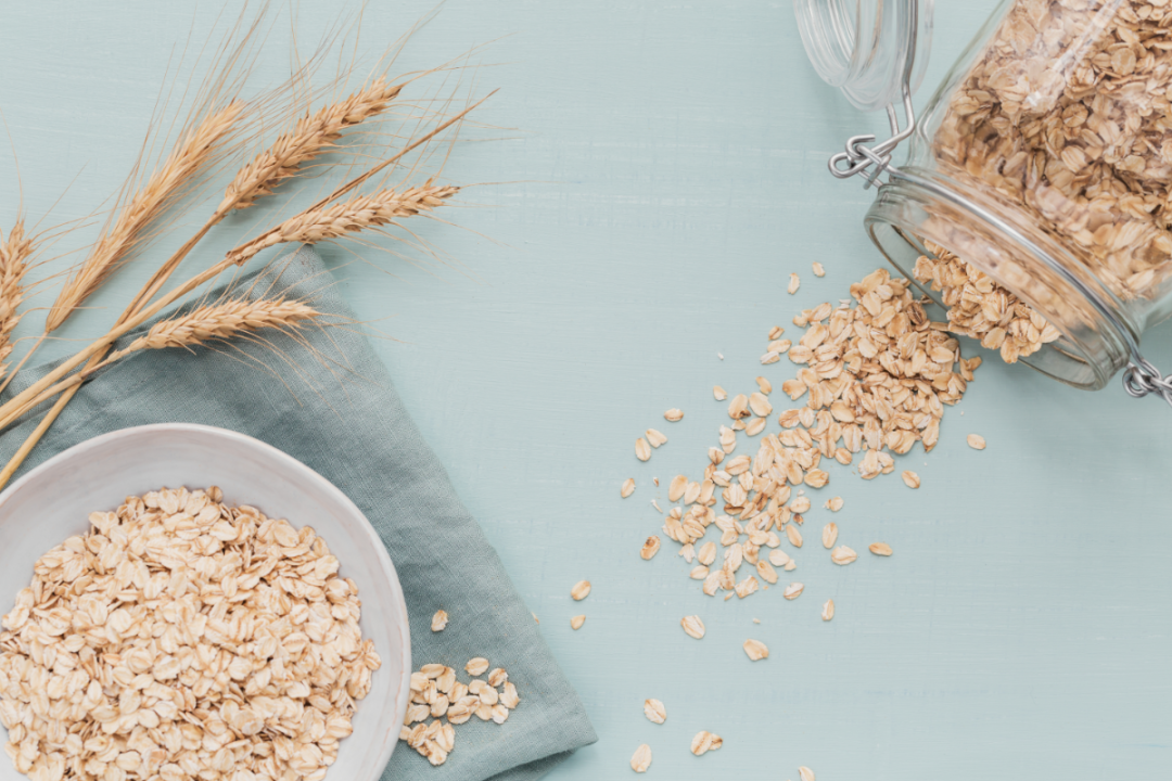 bowl of dry oat flakes with ears of wheat on light background