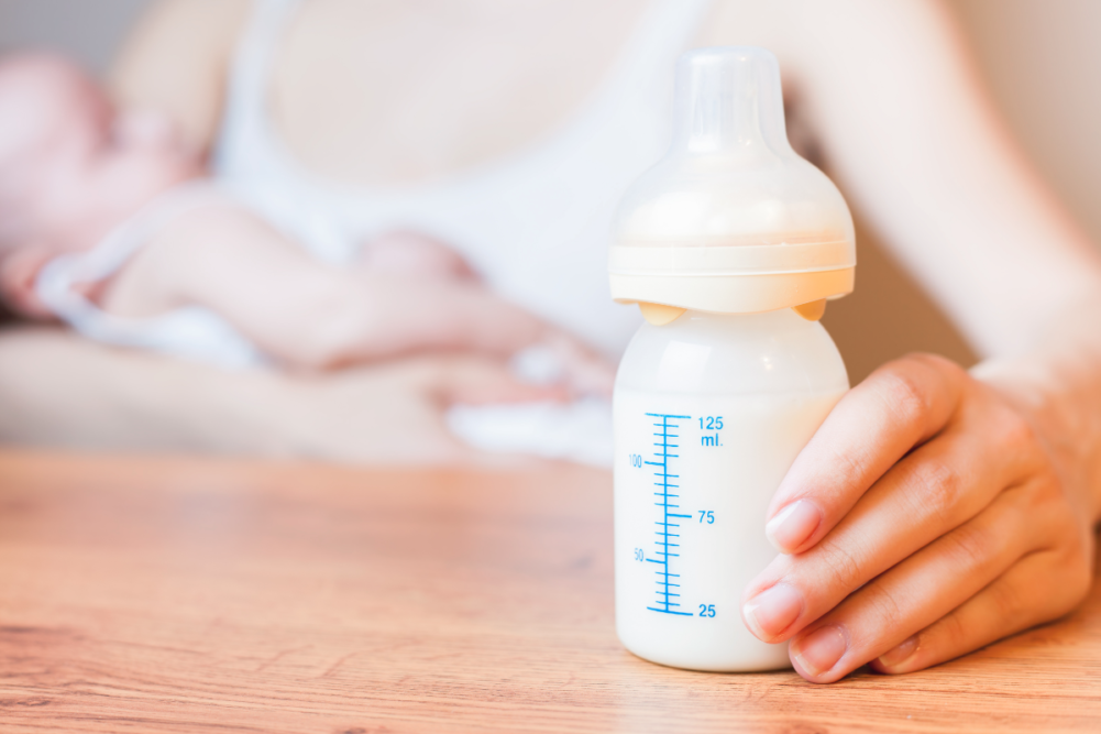bottle of infant formula next to a mother holding an infant  