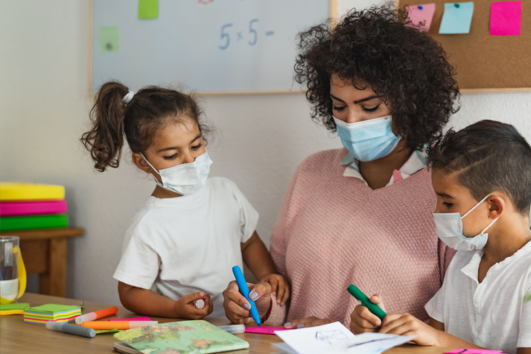 Teacher with children wearing face mask in preschool classroom during corona virus pandemic