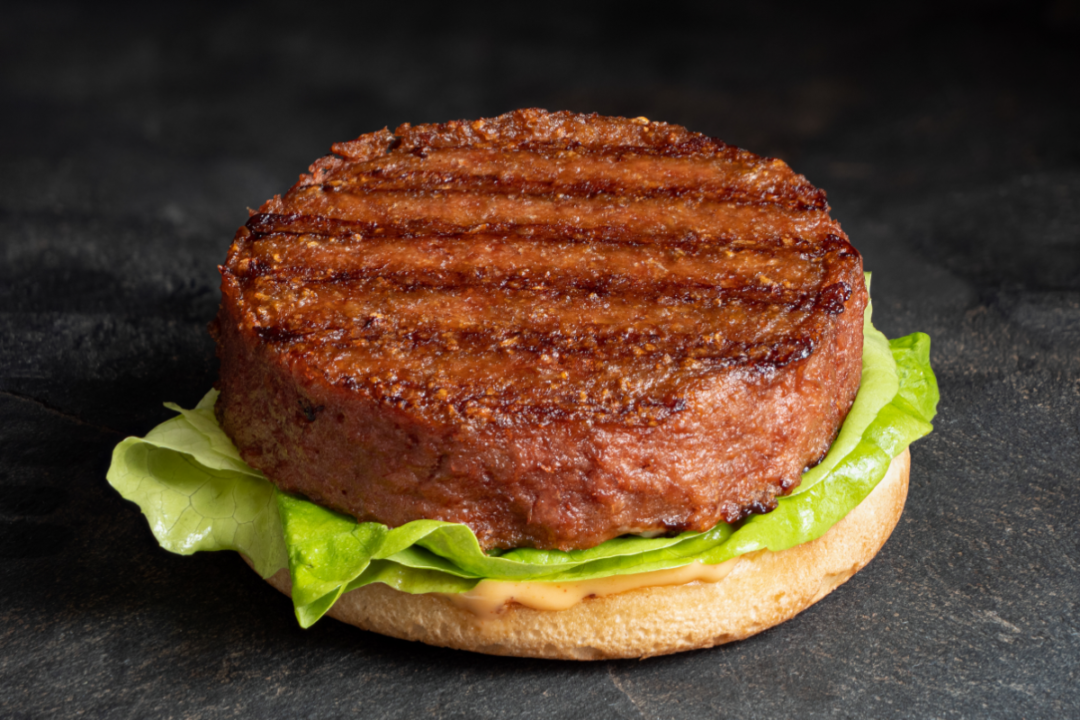 Freshly grilled plant based burger patty on bun with lettuce and sauce isolated on black countertop
