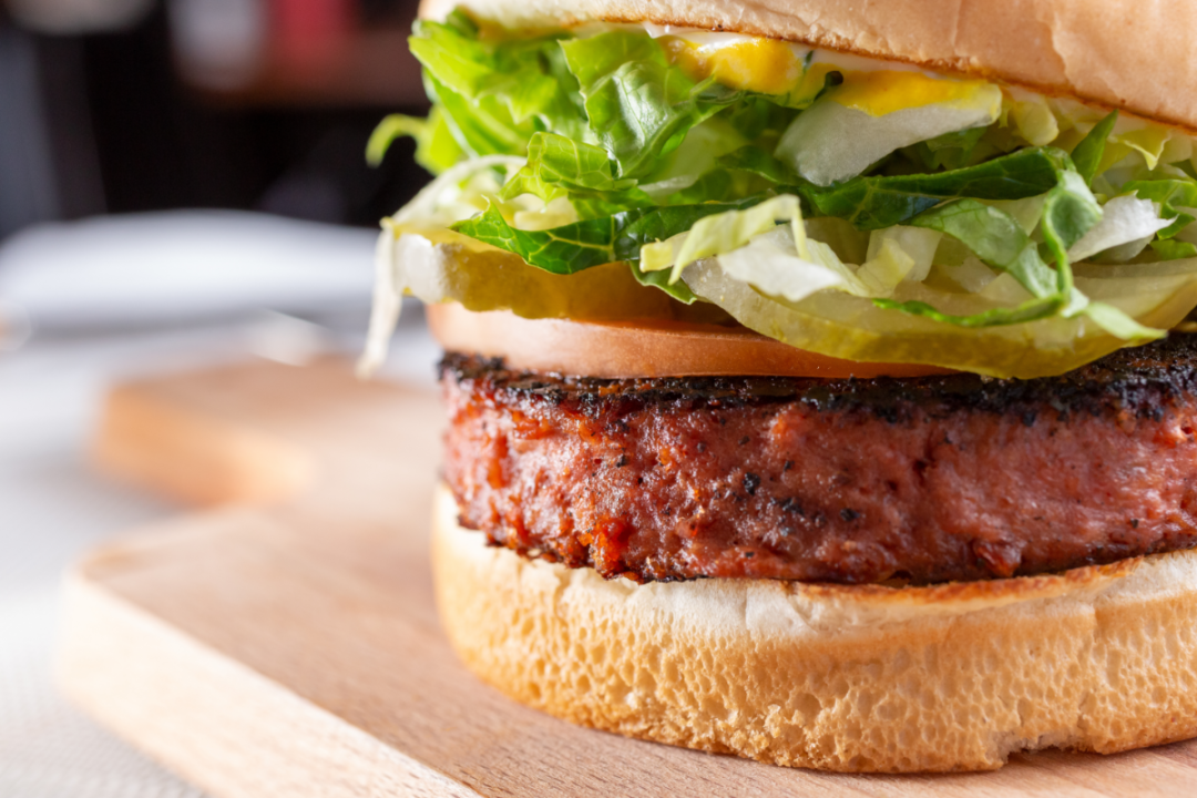 A closeup view of a burger, featuring a burger patty made of plant-based ingredients