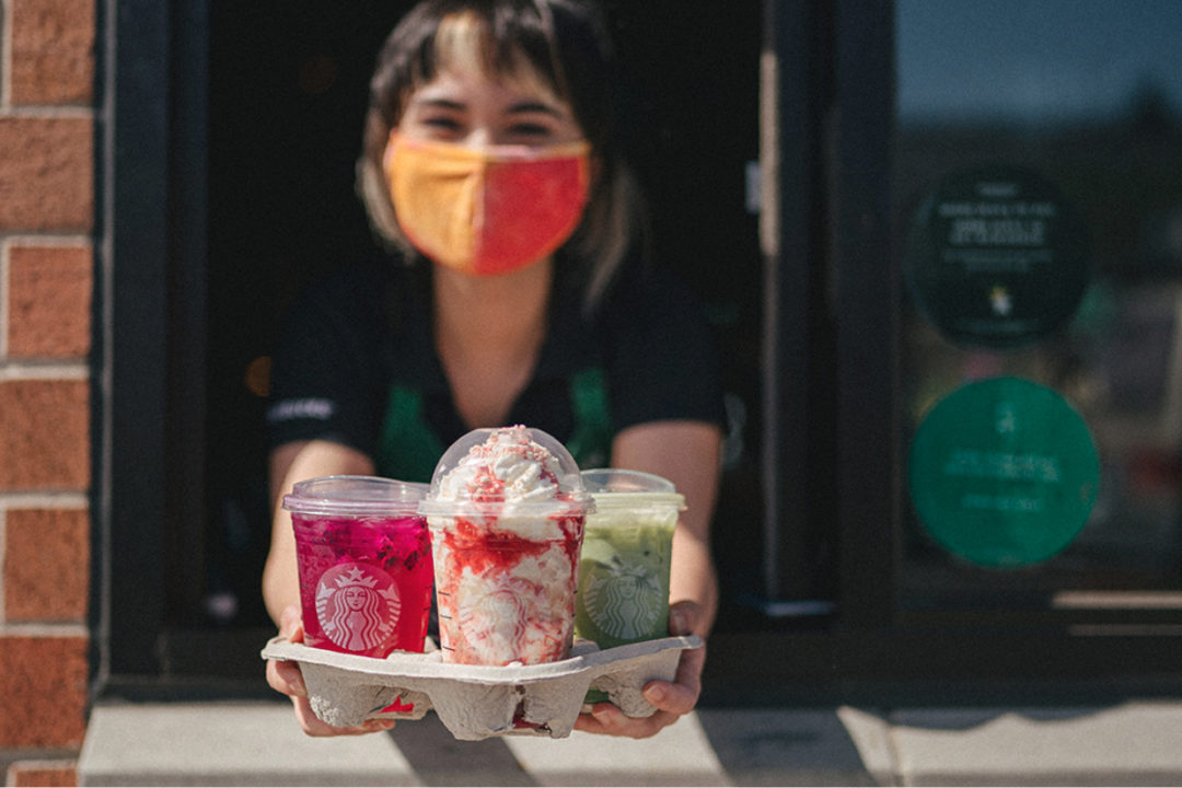 Starbucks employee wearing face mask delivering cold beverages at drive-thru