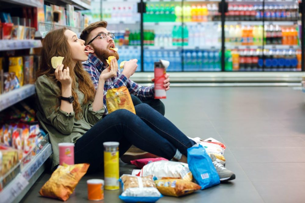 Couple sitting on supermarket floor eating snacks