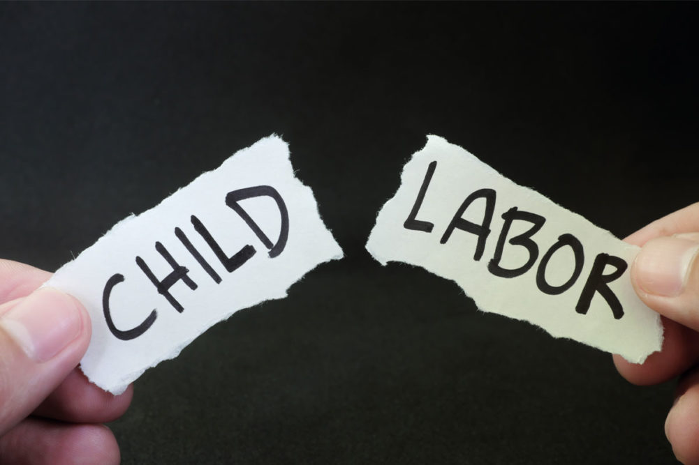 Hand tearing a piece of paper with 'child labor' written on it in two