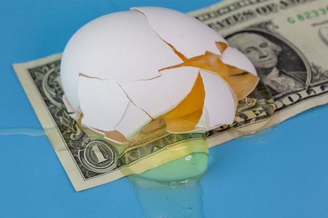 A broken egg on top of a dollar bill